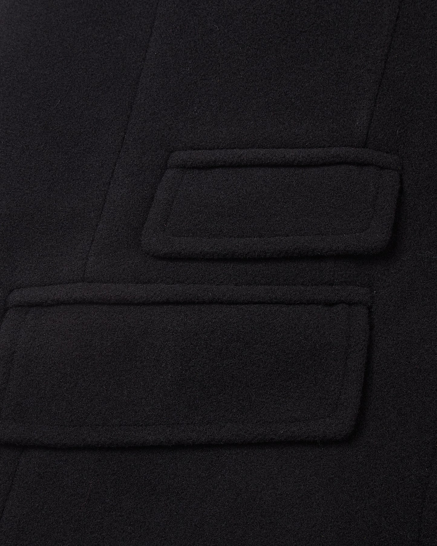 Detail of the double welt flap pockets on the black covert overcoat