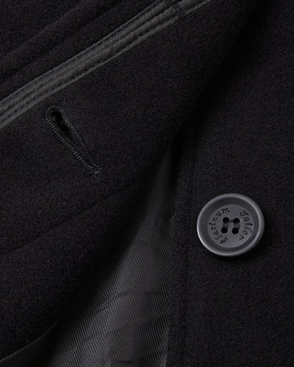 Detail of the concealed placket and dark button on the black overcoat